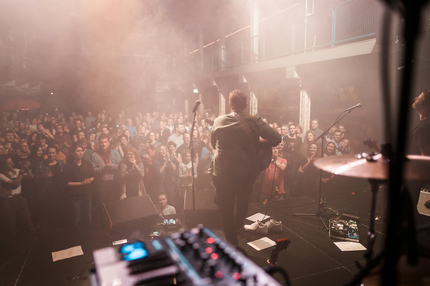 Musician playing guitar on stage for a clapping audience.