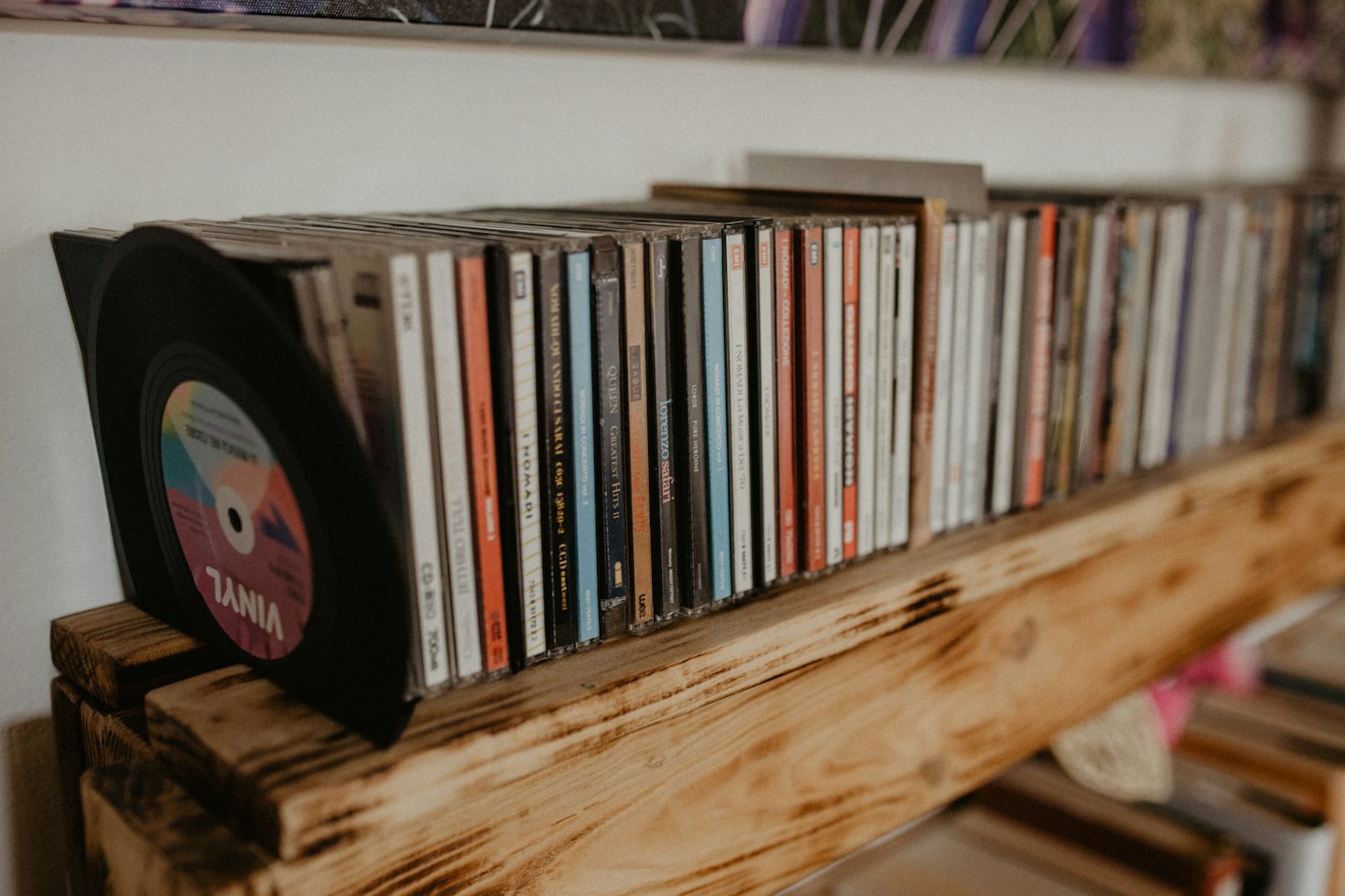 Music CDs and a vinyl record on a wooden shelf.