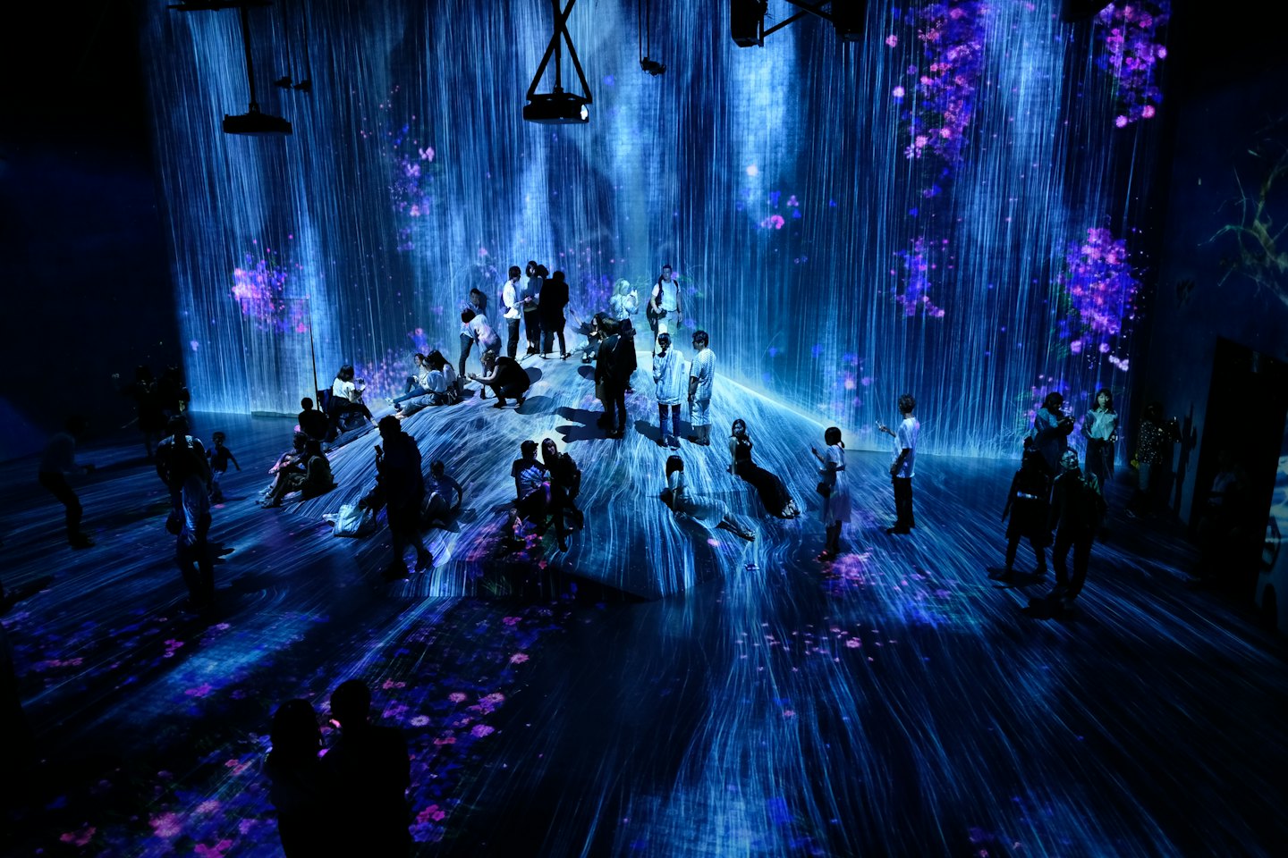 Visitors walk through a digital art exhibit featuring waterfall projections.