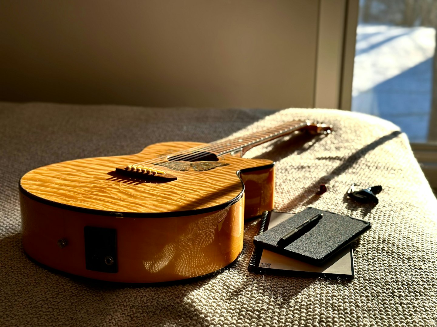 Acoustic guitar and notebooks resting on a textured beige blanket.